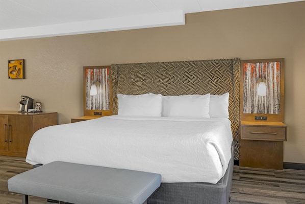 A hotel room with a large bed, a wooden nightstand, a bench, and a wall with abstract art. - Best Western Plus McCall Lodge & Suites (McCall)
