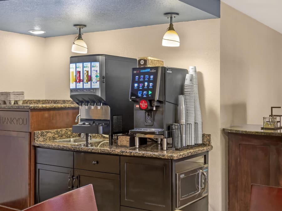 A self-service beverage station with a coffee machine, a refrigerated drink dispenser, and a coffee press.