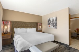 Habitación de hotel con una cama grande, un banco, una mesita de noche y una mesita auxiliar.