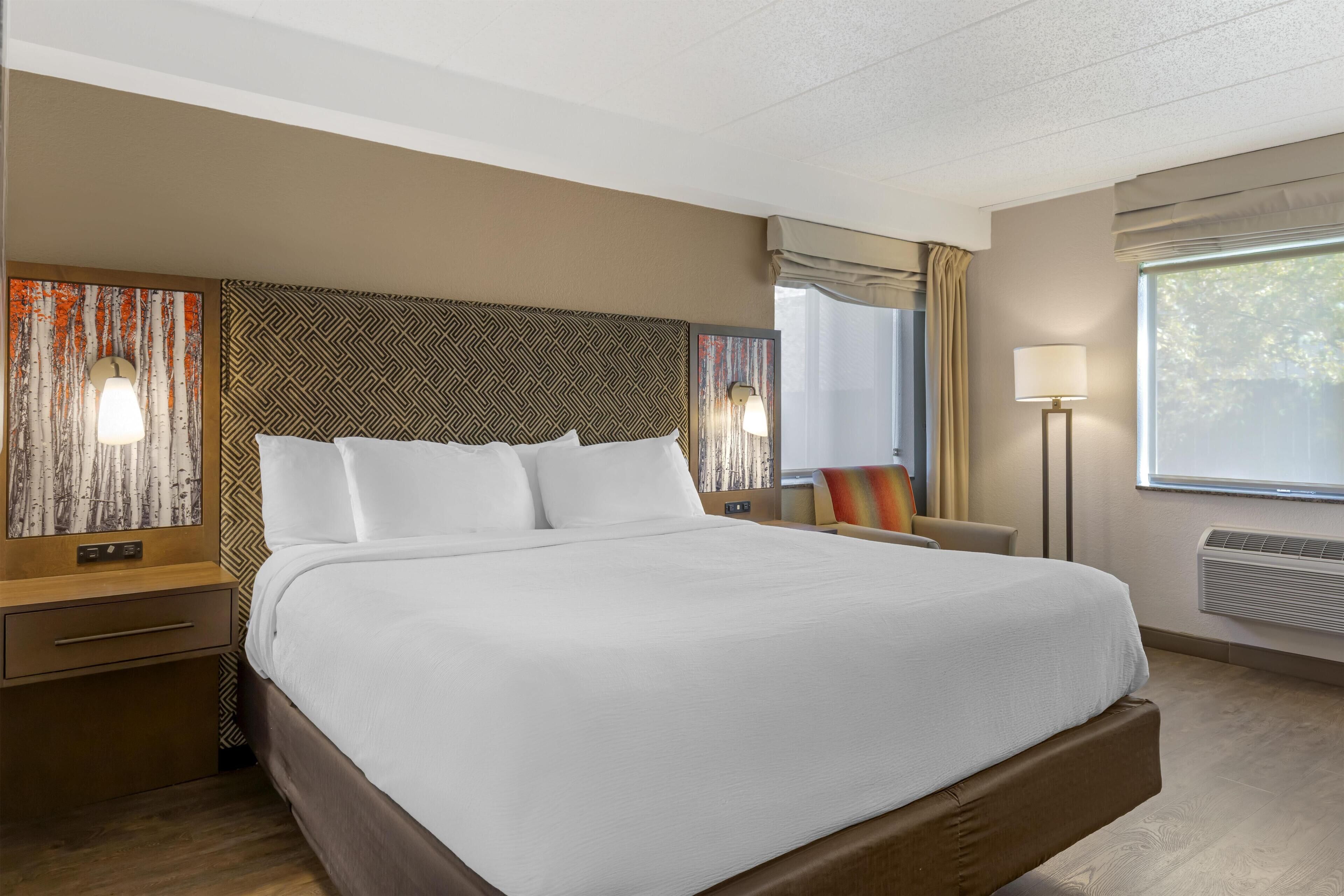 Een hotelkamer met een groot bed, een nachtkastje, een lamp en een raam met gordijnen.