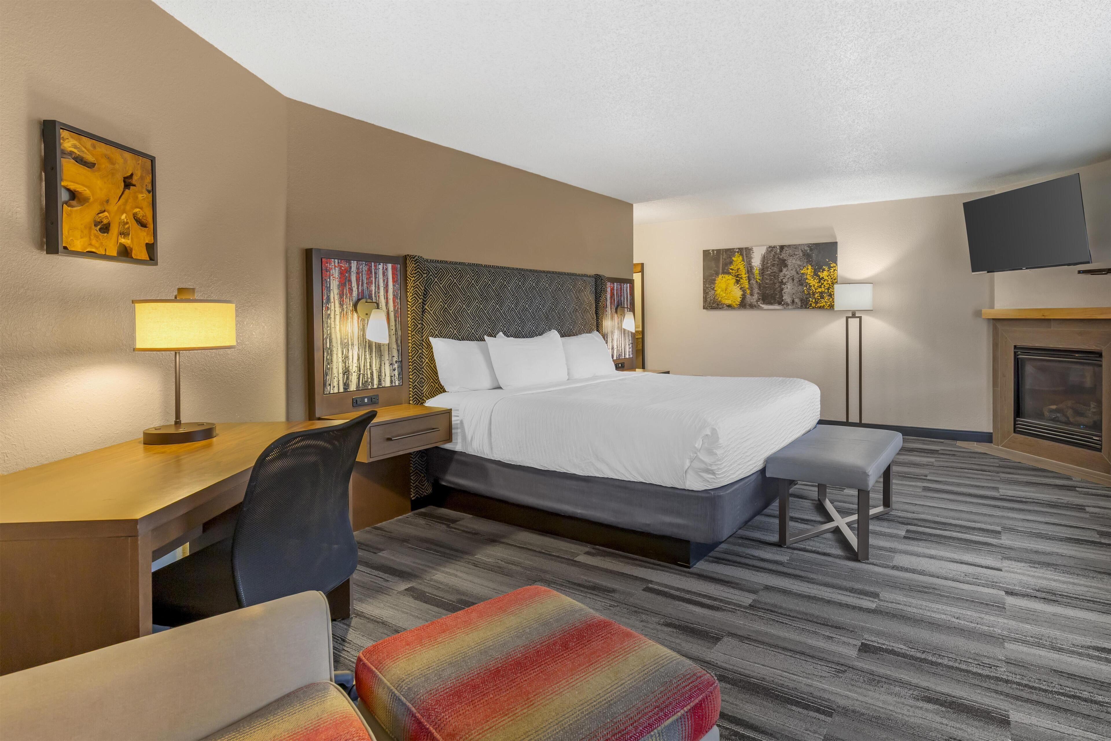 Quarto de hotel com cama, escrivaninha, cadeira, banco e obras de arte nas paredes.
