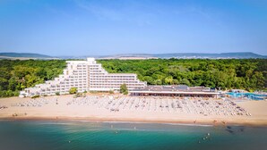 A large hotel with multiple floors and a beach area with numerous sunbeds and umbrellas.