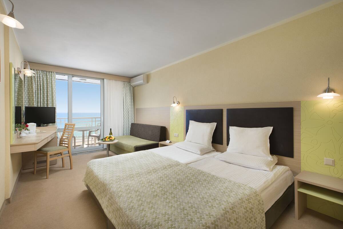 A hotel room with two beds, a desk with a chair, a small table, and a TV.