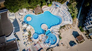 Vista aérea de un resort con una gran piscina con forma de coche, rodeada de zonas de descanso y tumbonas.