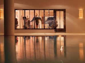 A gym with exercise equipment and a reflection in the pool. - Rocco Forte The Charles Hotel (Munich)