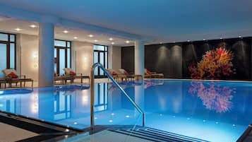 An indoor swimming pool with clear water, a glass barrier, and a seating area with chairs and a table.