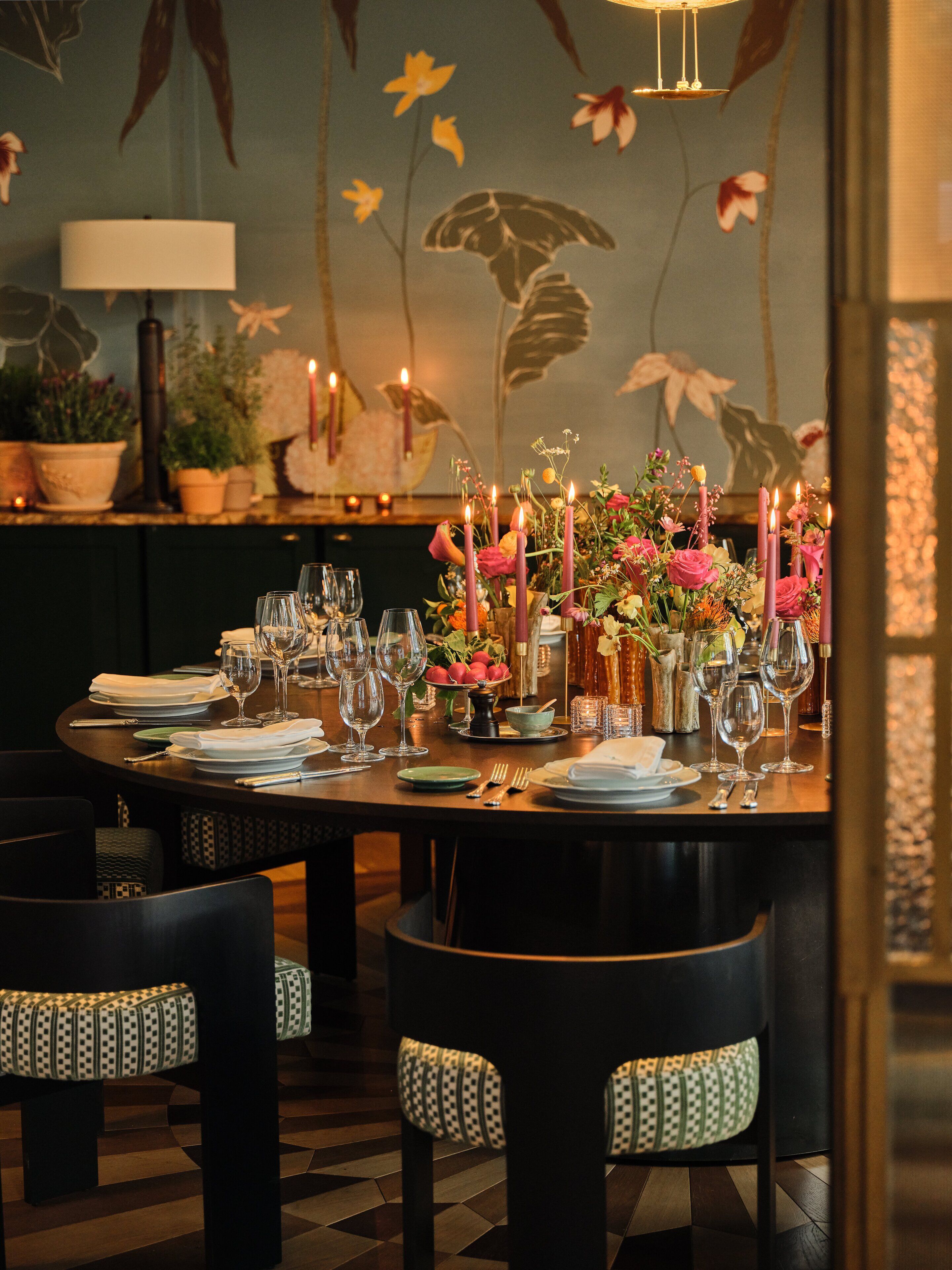 A dining table set with candles, glasses, and plates, surrounded by chairs with patterned cushions.