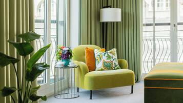 Una sala moderna con un sillón amarillo, una mesita de noche con un jarrón de flores y vistas a la ciudad a través de amplios ventanales.