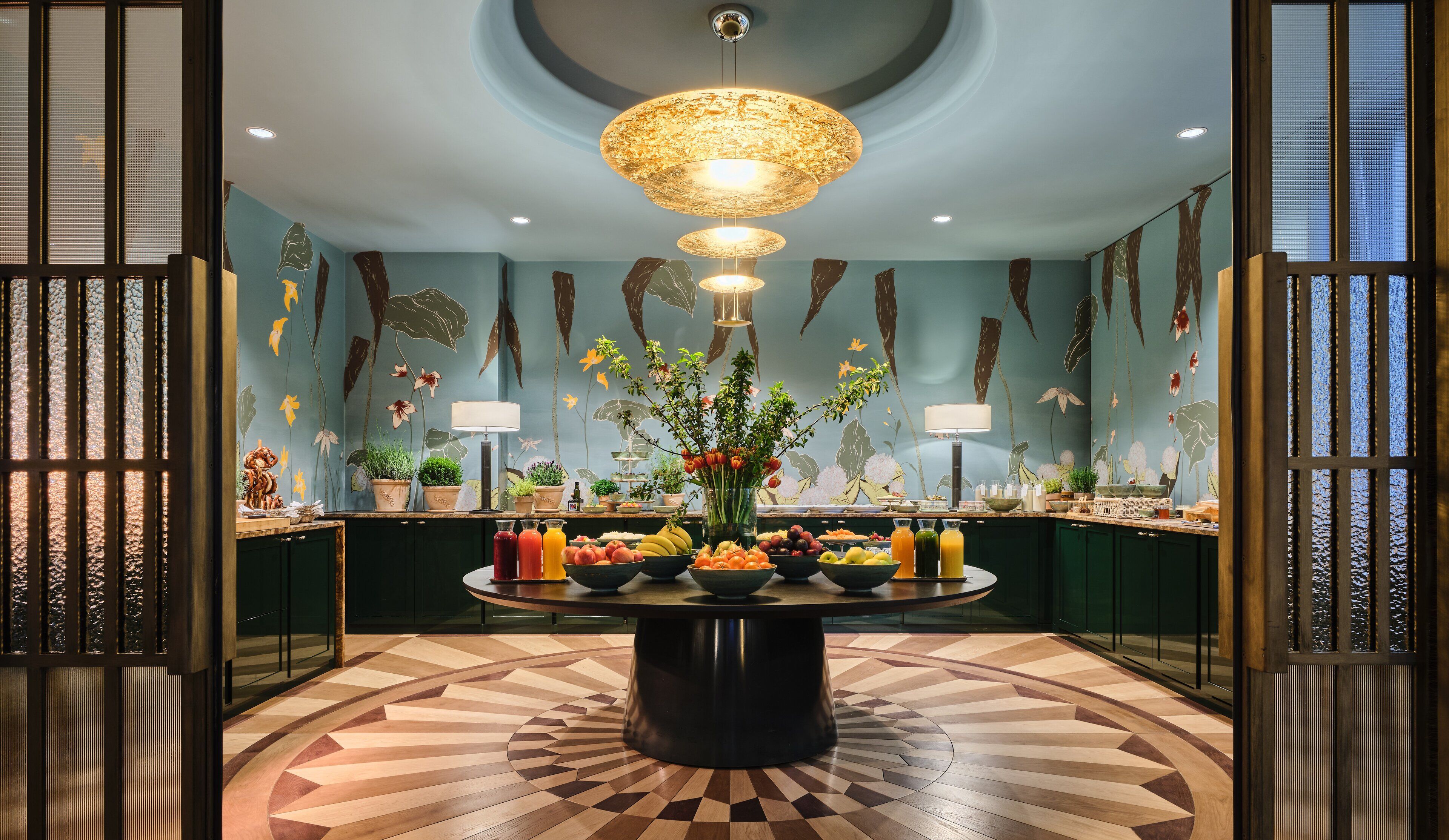 Een kamer met een ronde tafel in het midden, omringd door potplanten en diverse soorten fruit en drankjes.