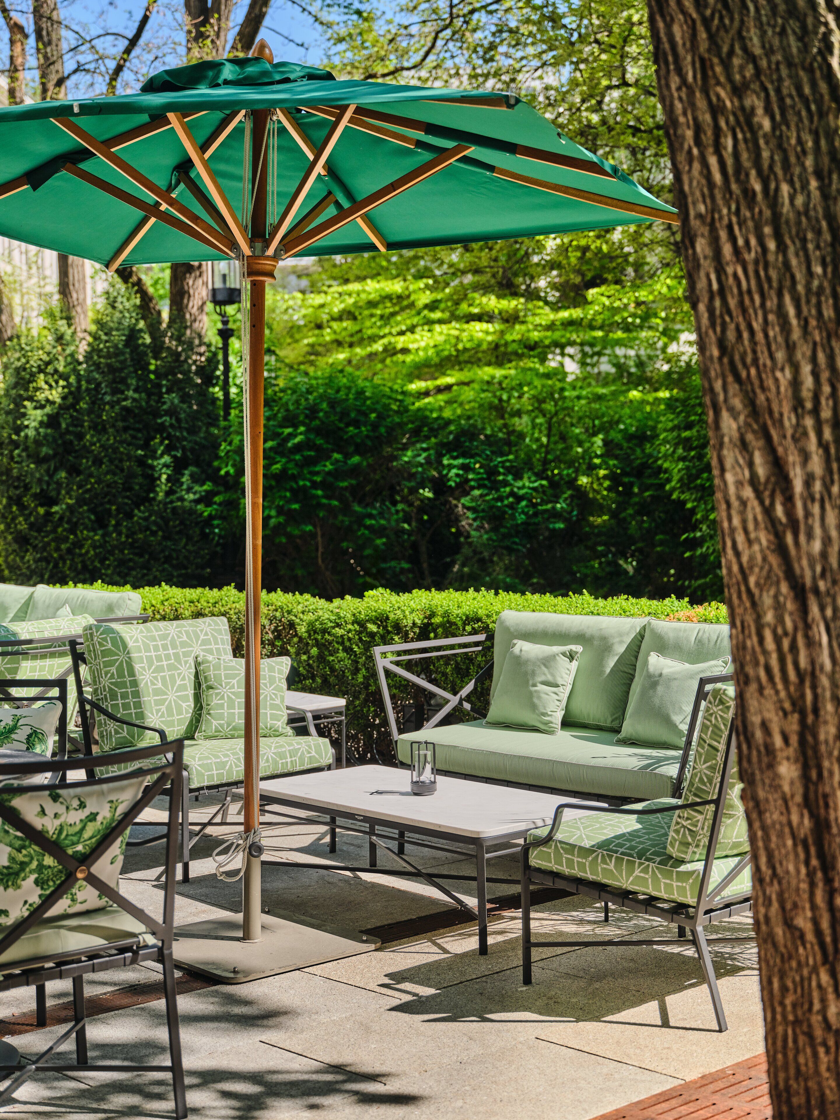 An outdoor patio area with a green umbrella, a cushioned sofa, and a metal table.