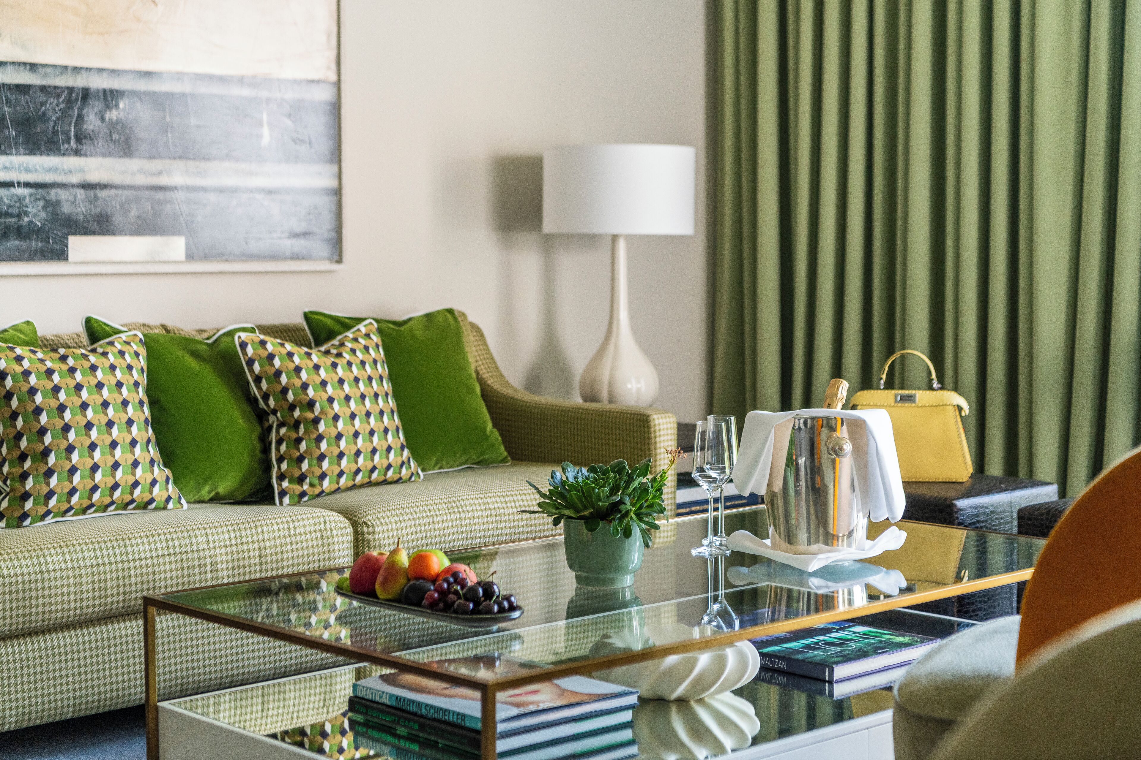 Un salon moderne avec un canapé, des coussins verts, une table basse en verre, une plante en pot et un sac à main jaune.