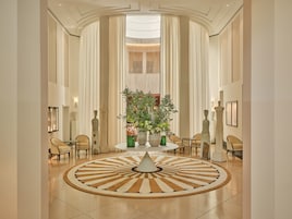 Un'ampia hall con un tappeto circolare al centro, alte finestre e un'abbondante composizione floreale.
