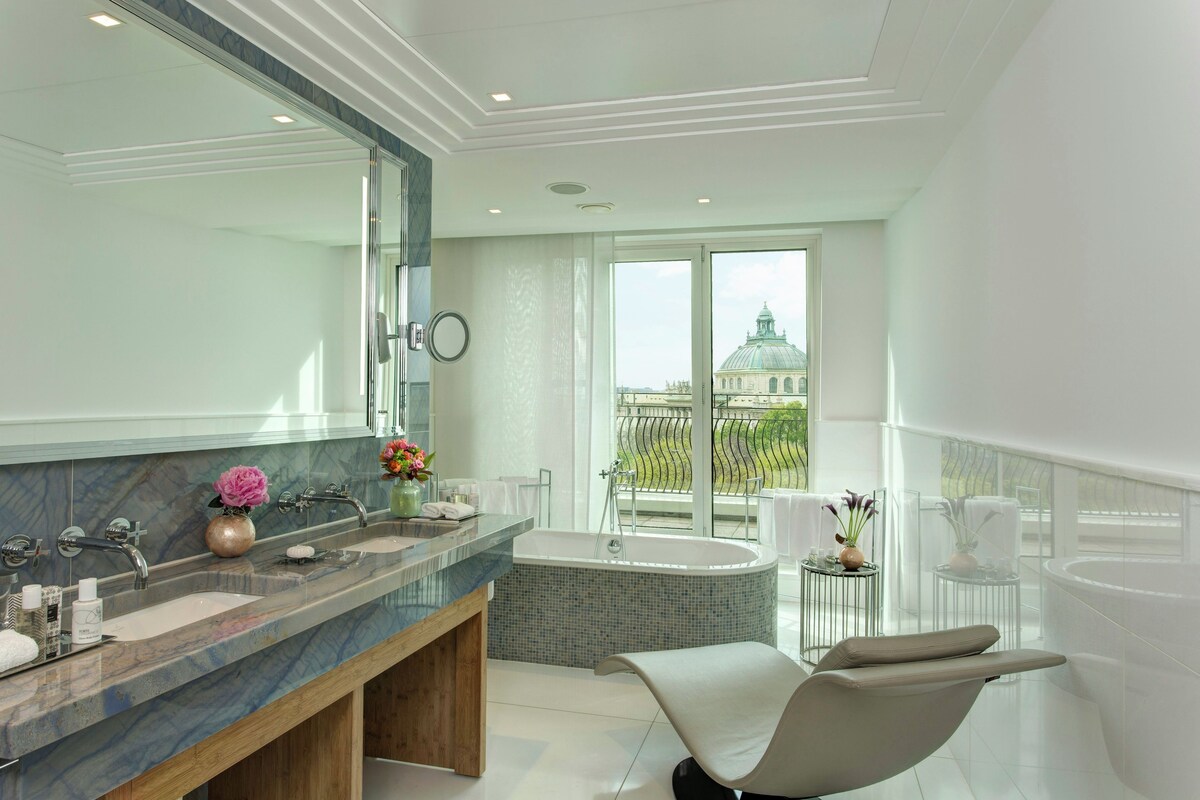 Ein modernes Badezimmer mit einem großen Spiegel, zwei Waschbecken, einer Badewanne und Blick auf ein Gebäude durch das Fenster.