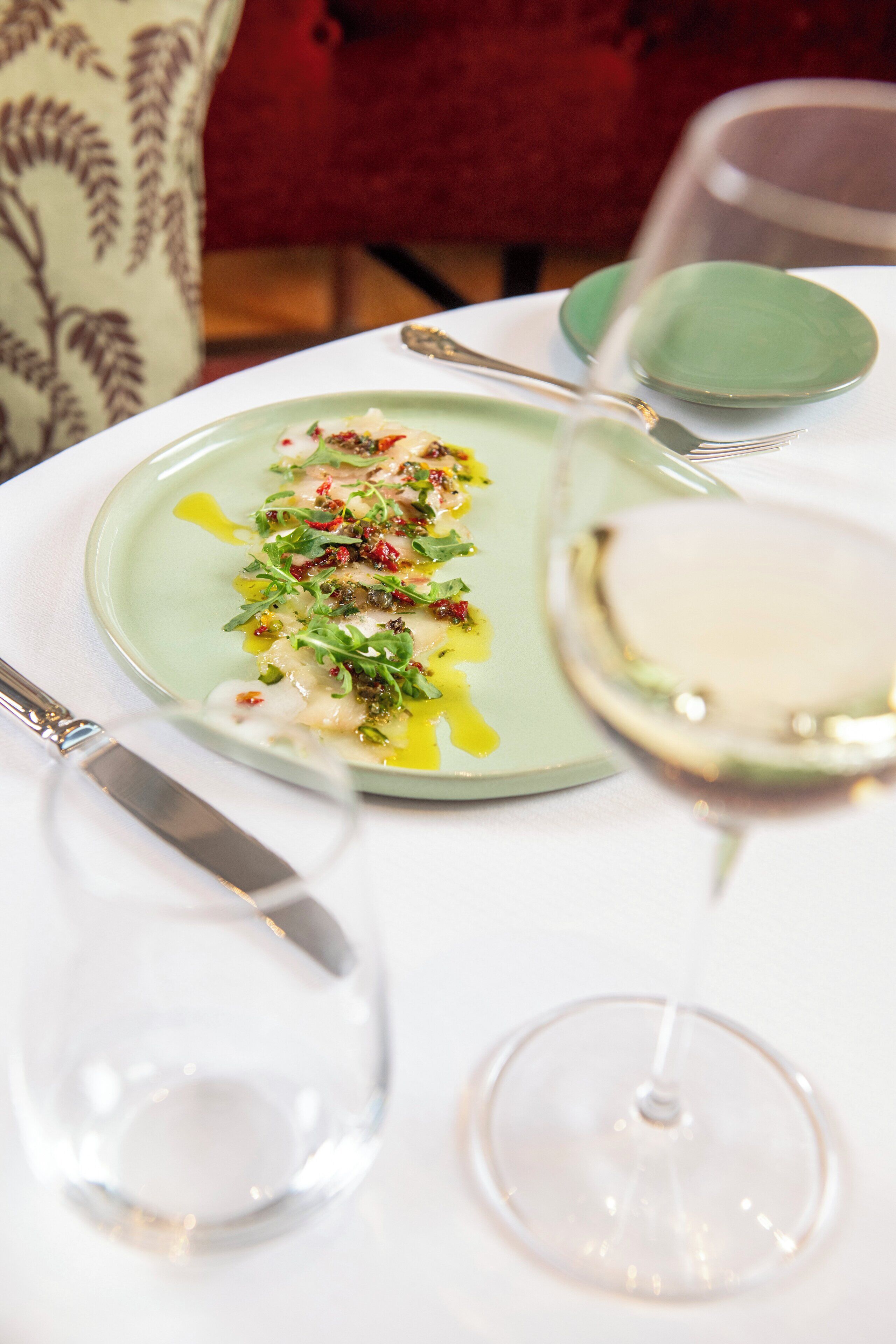 Una mesa de comedor con un plato de comida, una copa de vino y un plato verde.