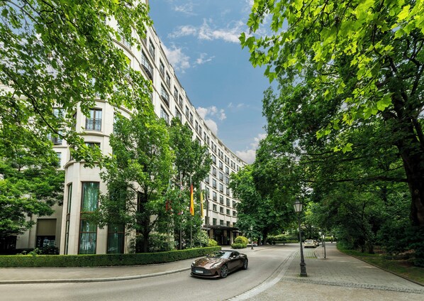 Una calle arbolada con un edificio moderno, un coche aparcado y un farol.