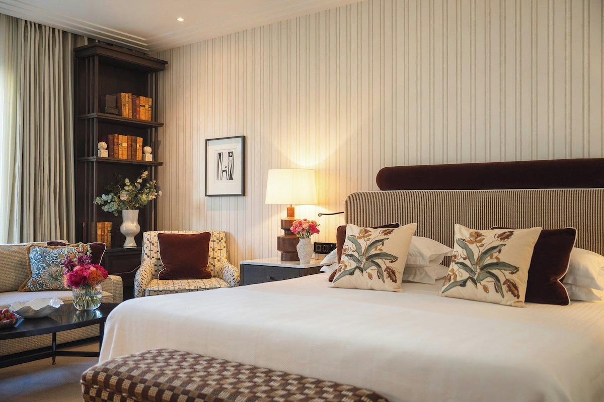 A hotel room with a large bed, a bookshelf, a desk, and a chair.