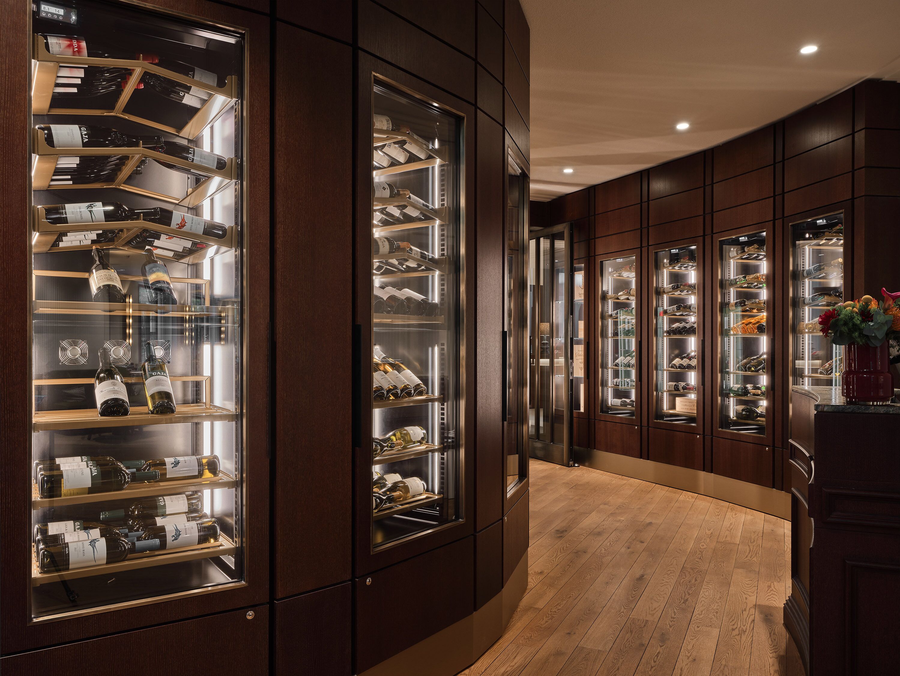 Un pasillo de hotel de lujo con paneles de madera y vitrinas de vidrio que exhiben vino y zapatos.