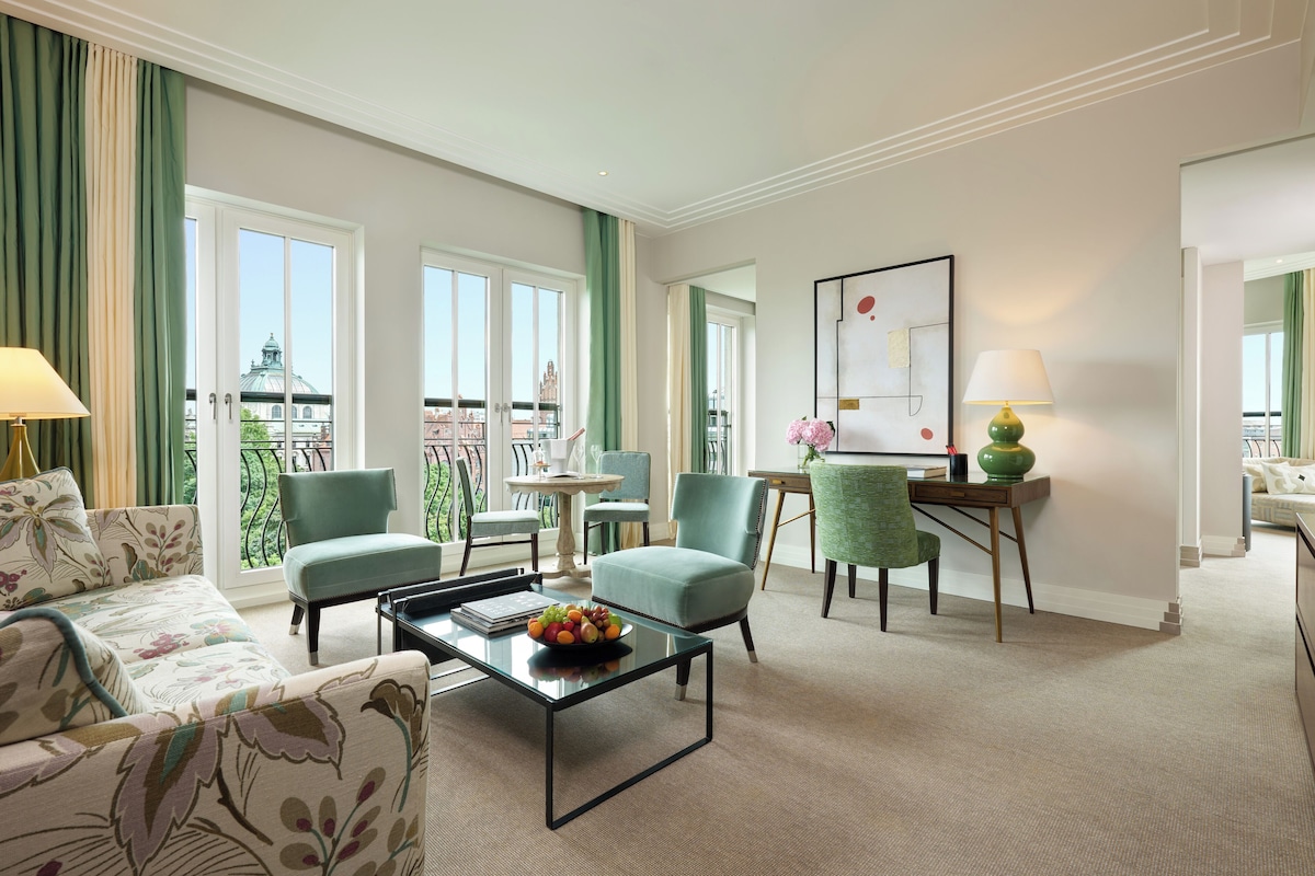 A hotel room with a balcony, a sofa, a dining table, and a desk with a chair.