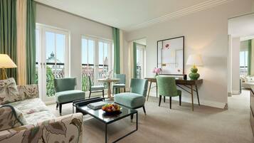 A hotel room with a balcony, a sofa, a dining table, and a desk with a chair.
