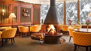 Habitació acollidora amb una llar de foc, revestiment de fusta i vista a muntanyes cobertes de neu.