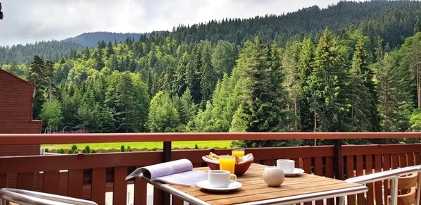 A wooden deck with a table set for breakfast, overlooking a forested mountain. - Yastrebets Wellness & Spa (Samokov)