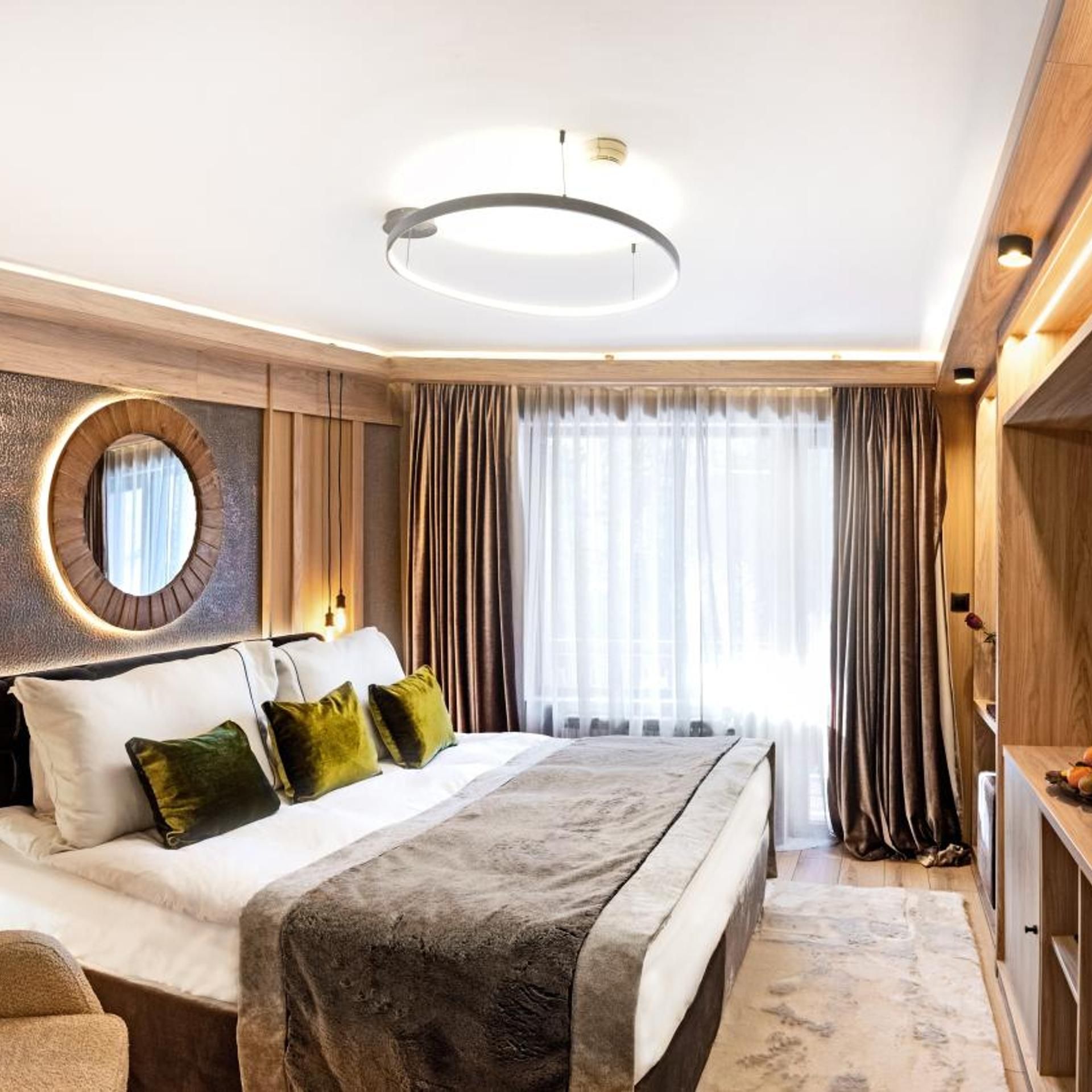 A modern hotel room with a large bed, a round mirror, a ceiling light, and a view of the outdoors.