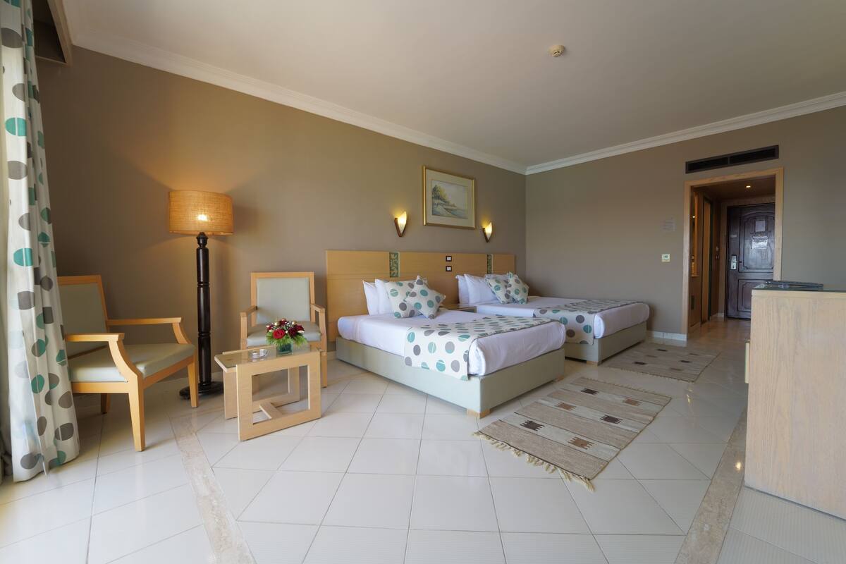 Een hotelkamer met twee bedden, een bureau, een stoel, een lamp en een schilderij aan de muur.