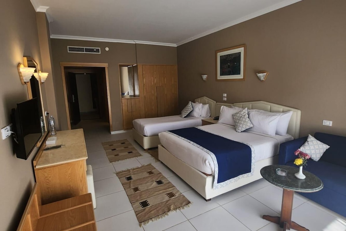Una habitación de hotel con una cama, un sofá, una mesita, un televisor y un armario de madera.