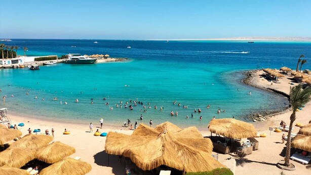 A beach with thatched umbrellas, a sandy shore, and clear blue water. - Regina Resort & Aqua Park Hurghada (Hurghada)