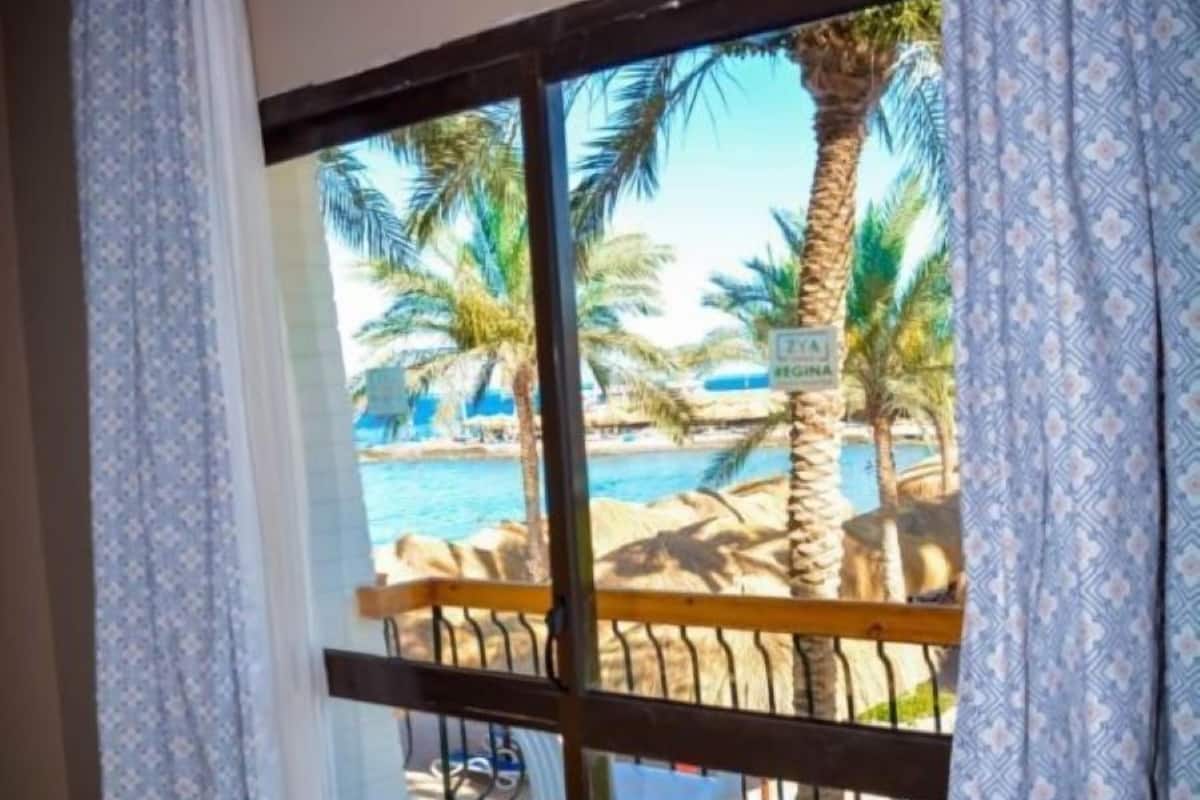 Een kamer met uitzicht op een strandresort, met een zwembad, palmbomen en strandstoelen.