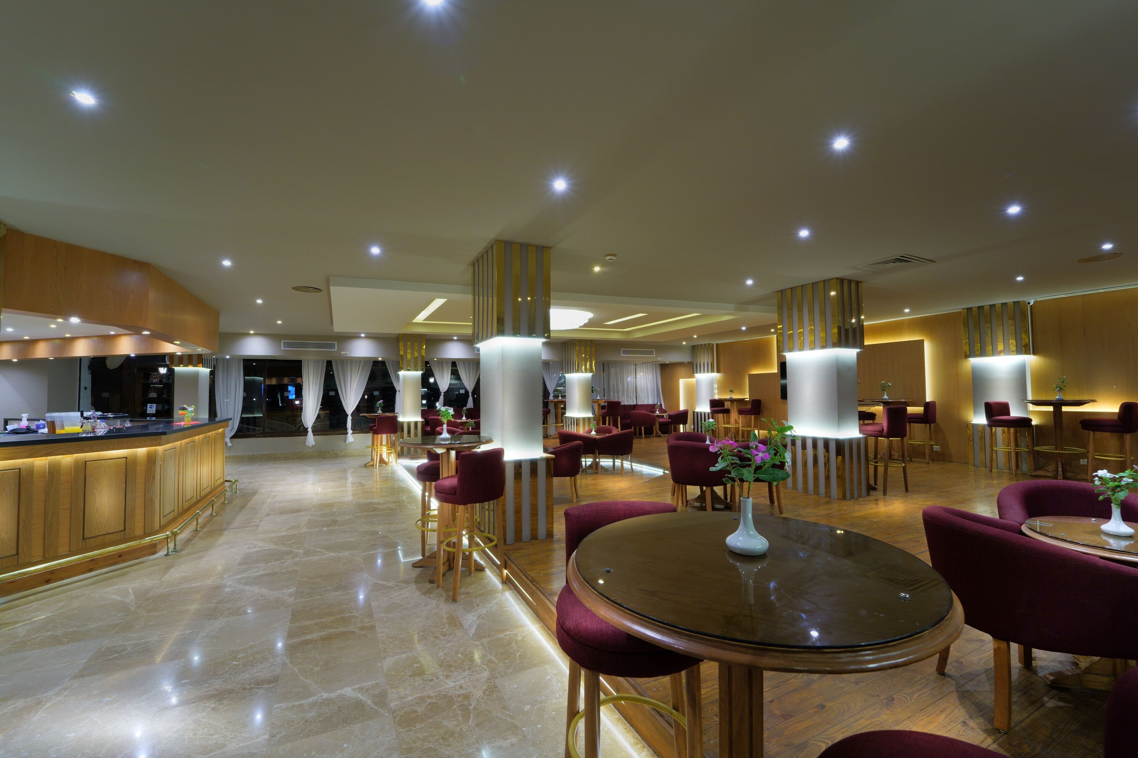 A spacious hotel lobby with a central bar area, multiple seating arrangements, and modern lighting fixtures.