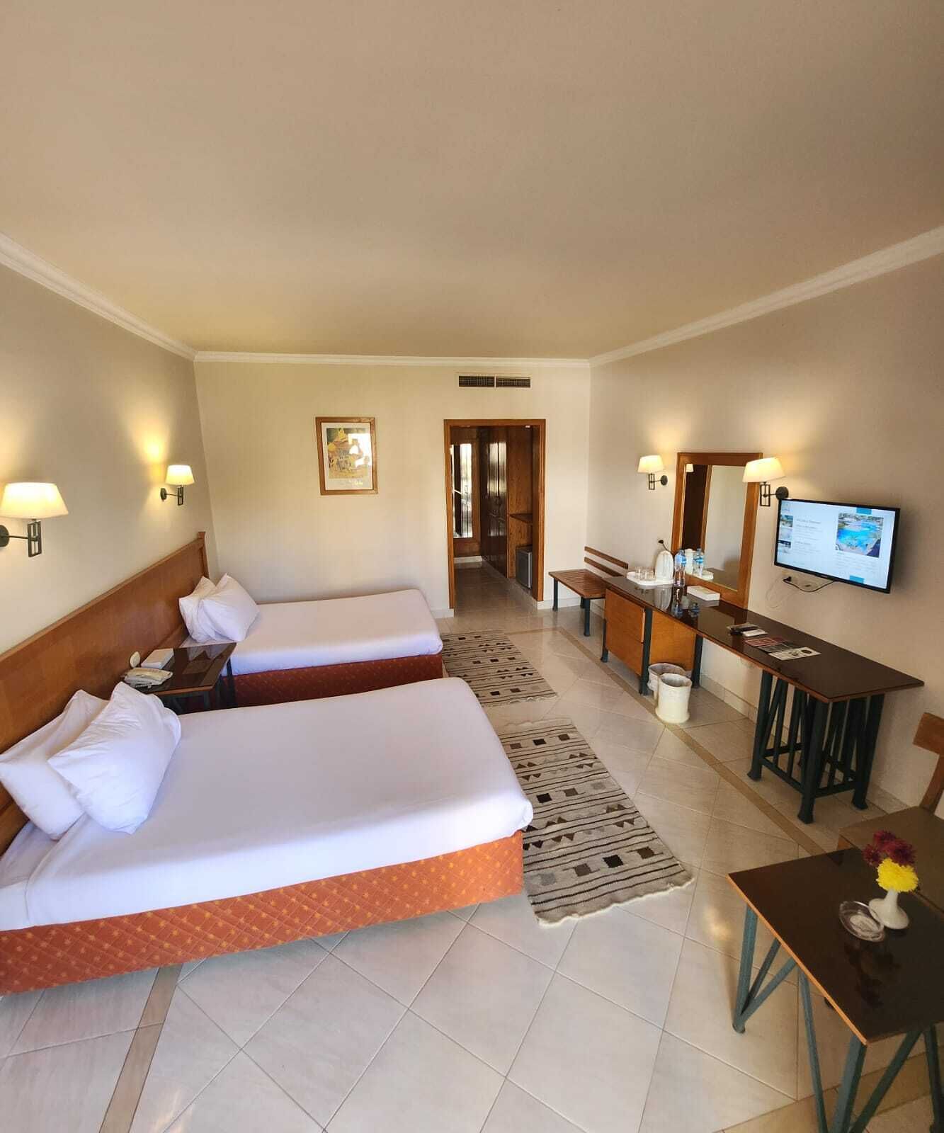 Une chambre d’hôtel avec deux lits, un bureau avec une chaise, une télévision et une salle de bain visible à travers une porte ouverte.