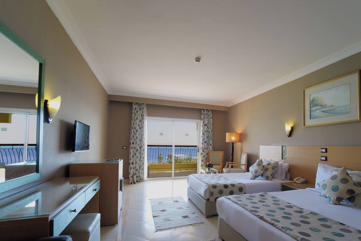 Een hotelkamer met twee bedden, een bureau, een stoel, een televisie en een balkon met uitzicht.