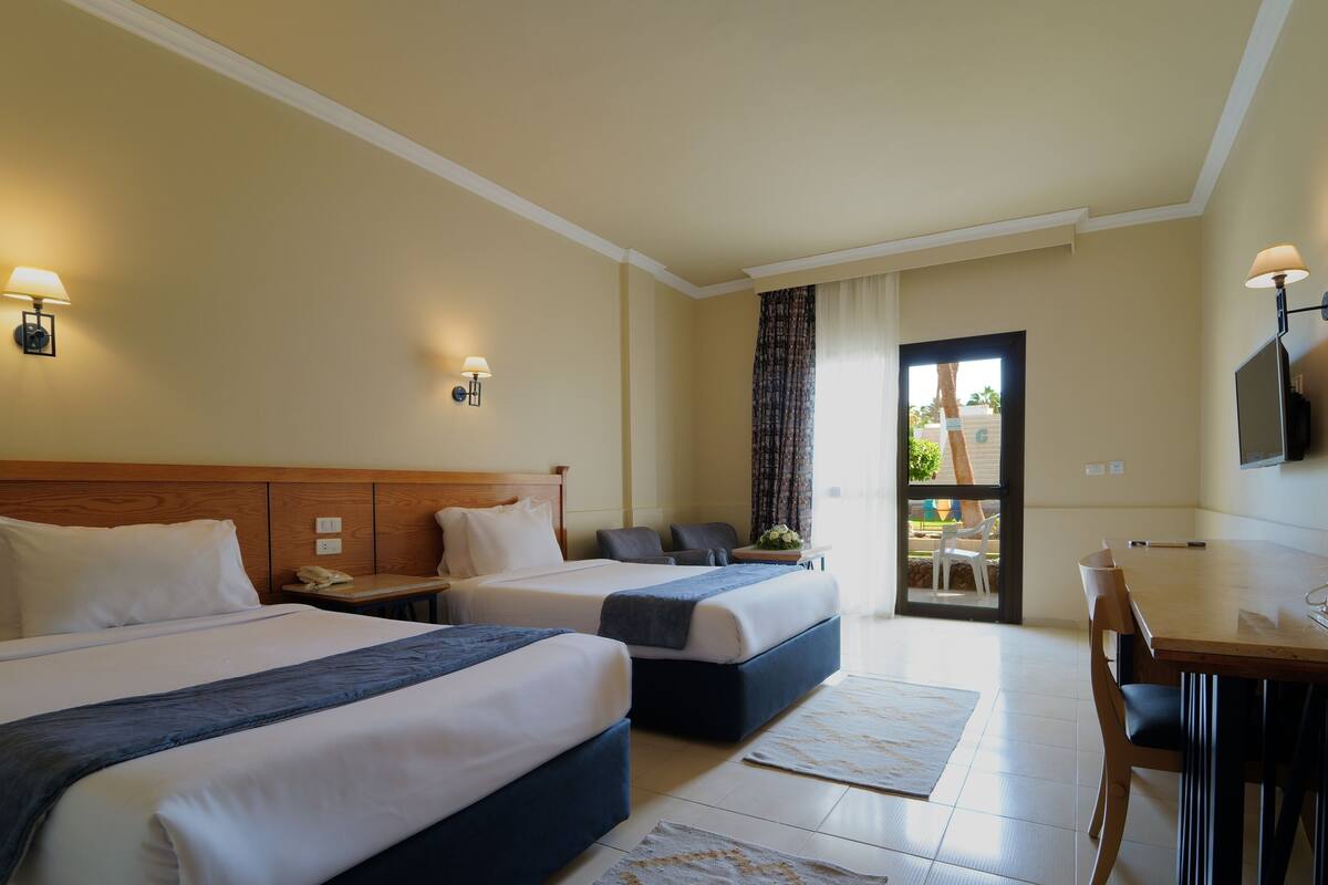 Hotelkamer met twee bedden, een bureau en een stoel. Er zijn wandlampen en een raam met gordijnen.