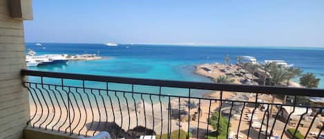 Ein Balkon mit Blick auf das Meer, einen Sandstrand und ein kleines Gebäude.
