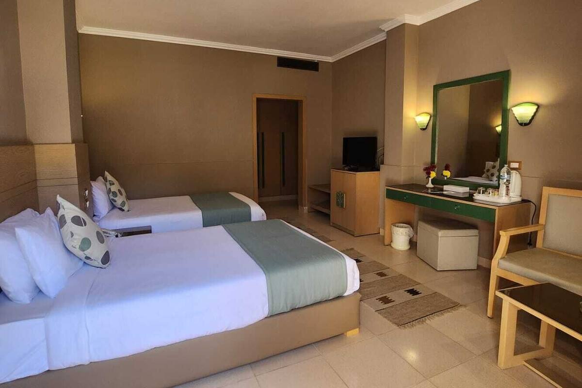 Een hotelkamer met twee bedden, een bureau, een stoel, een spiegel en een televisie.