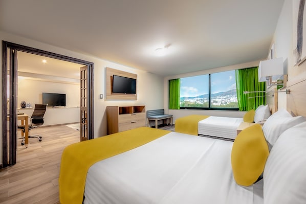 A hotel room with a bed, a desk, a chair, a TV, and a window with a view of a cityscape.