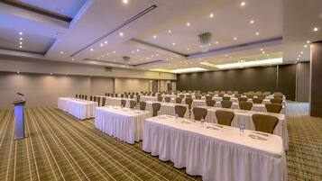 A conference room with rows of tables and chairs, a podium, and a carpeted floor.