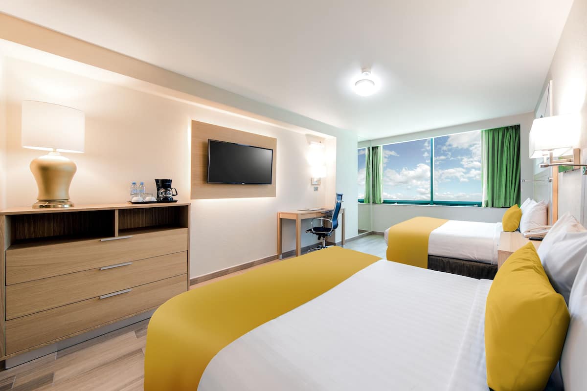 Une chambre d’hôtel avec deux lits, un bureau, une chaise, une télévision et une fenêtre avec des rideaux.