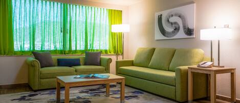 A modern living room with two green sofas, a wooden coffee table, and a lamp on a side table.