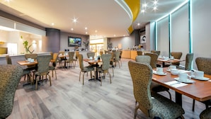 A modern dining area with round tables and cushioned chairs, a television, and a bar area in the background. - La Joya Pachuca (Pachuca)