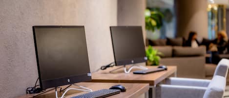 Two HP desktop computers on wooden desks in a modern office setting with grey chairs and a plant in the background.