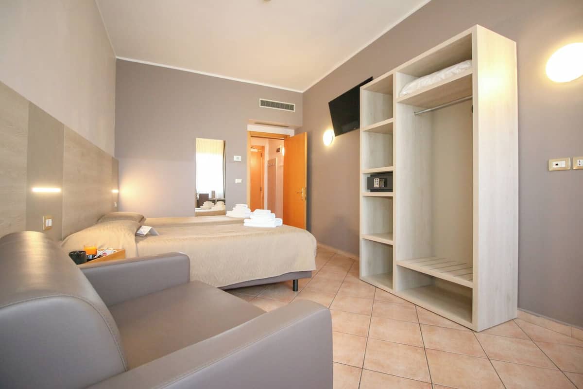 A hotel room with a bed, a seating area, a wardrobe, and a television.