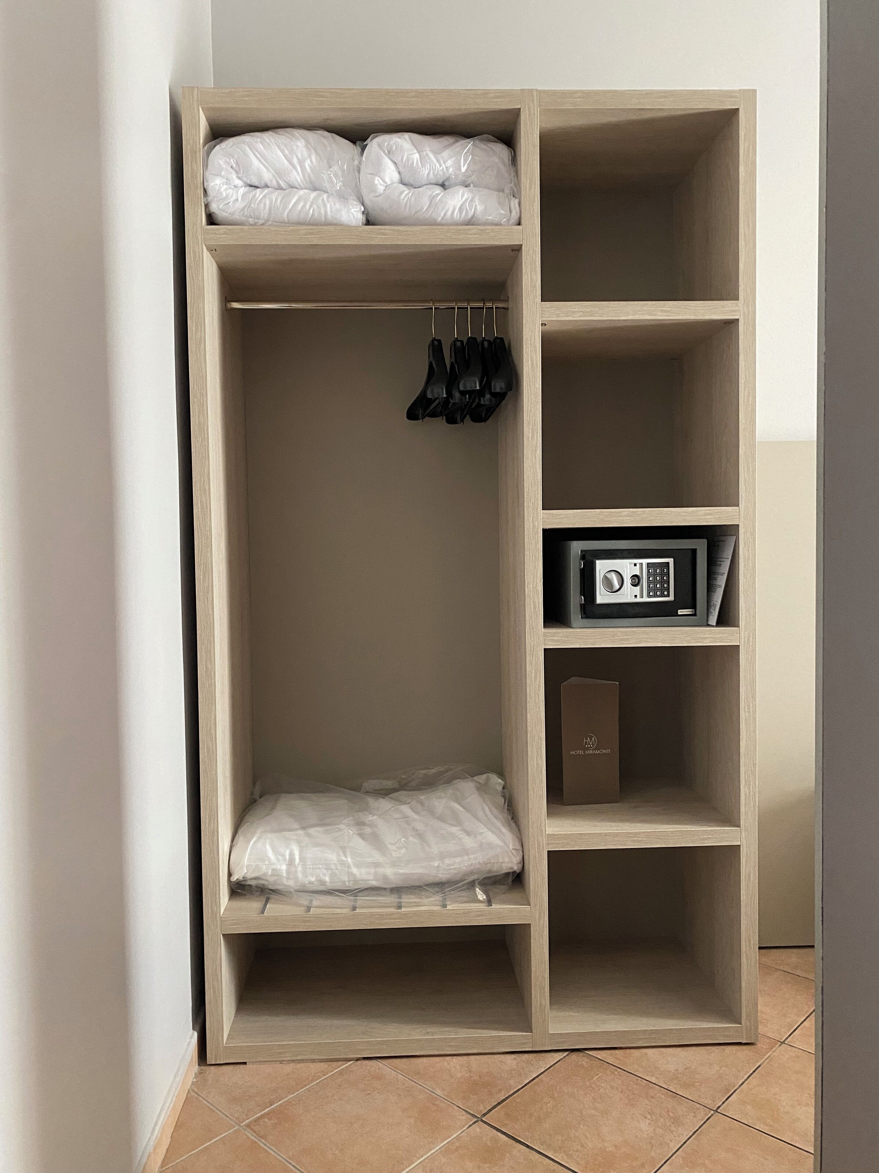 Un armario con dos repisas, una con ropa doblada y la otra con una caja y un pequeño dispositivo electrónico.