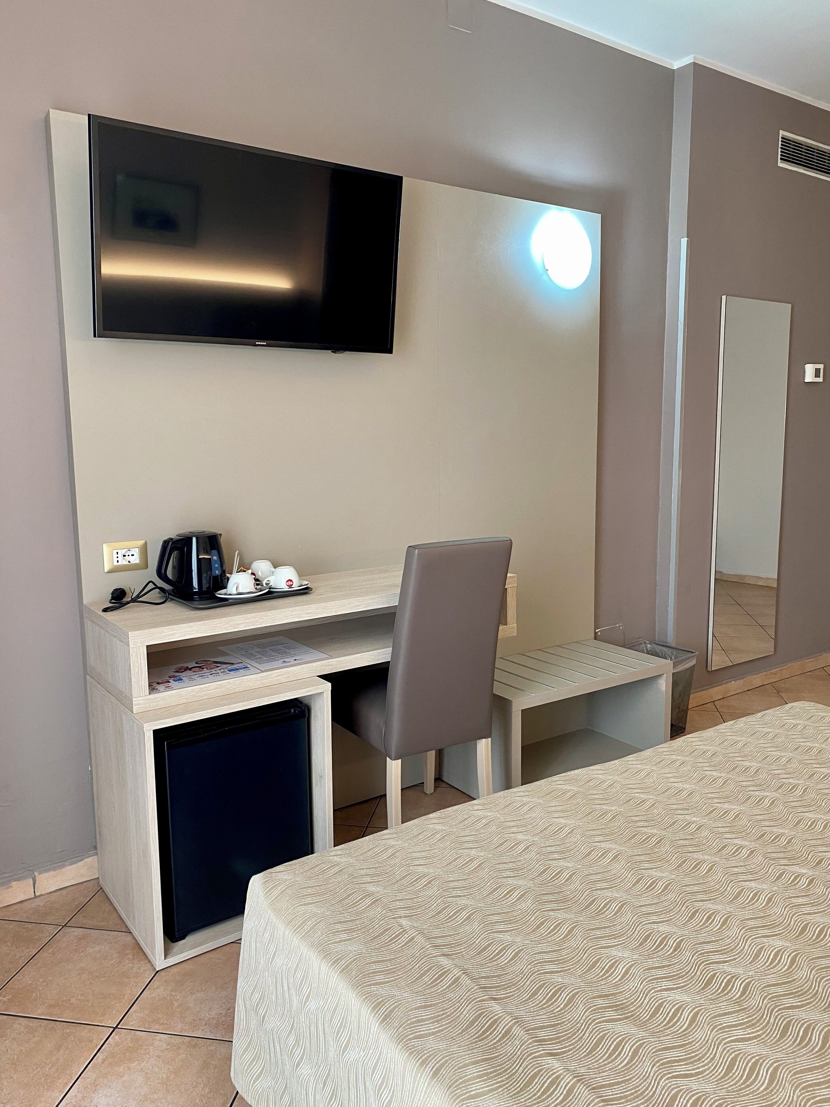 Una habitación de hotel con una cama, un escritorio con una silla, un televisor y un espejo.