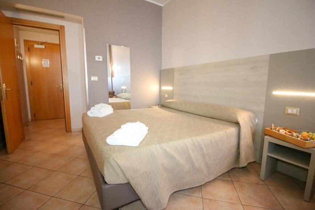 Ein Hotelzimmer mit einem Bett, einem Nachttisch mit Obstplatte, einem Spiegel und einer Tür zu einem anderen Raum.