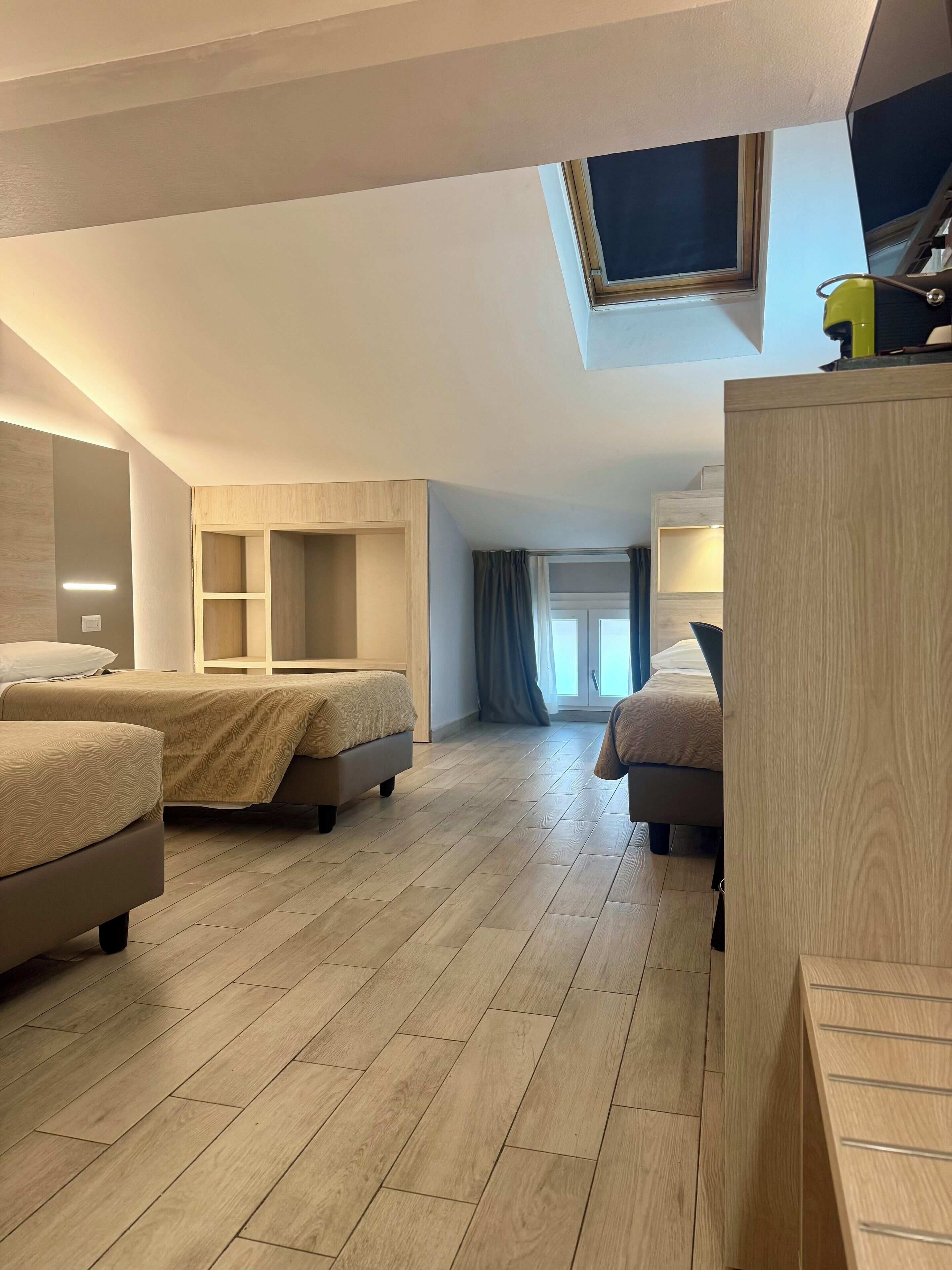 A modern hotel room with two beds, a skylight, and a wooden floor.