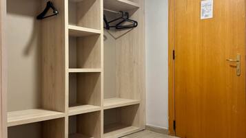 A walk-in closet with multiple shelves and hanging space, a wooden door, and a herringbone-patterned floor.