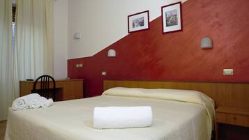 A hotel room with a large bed, a wooden nightstand, a desk, and two wall-mounted lamps.