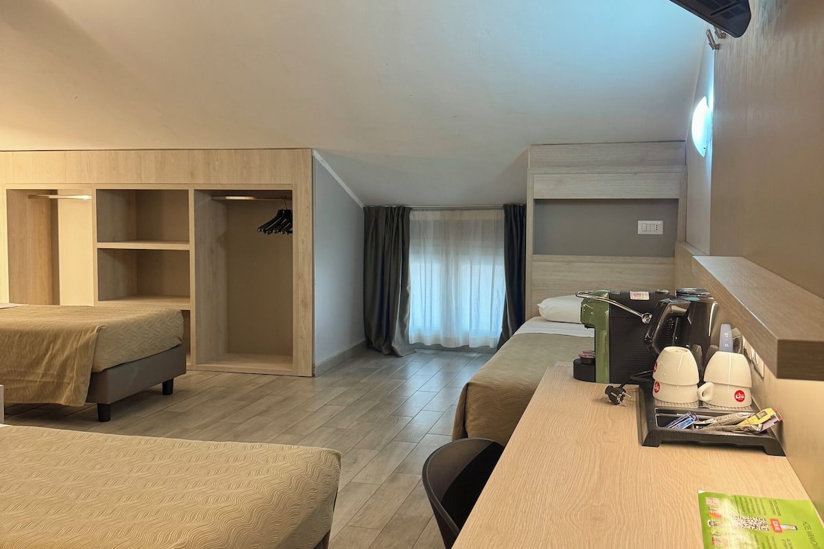 A hotel room with a bed, a desk, a coffee machine, and a TV mounted on the wall.